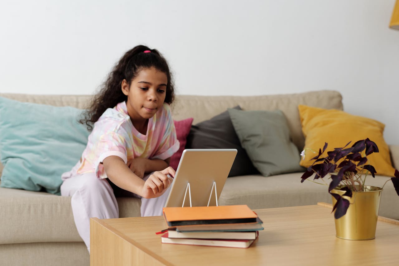 The Art of Drawing Readers In: Your attractive post title goes here A young girl using a tablet for online learning at home, sitting comfortably on a couch.