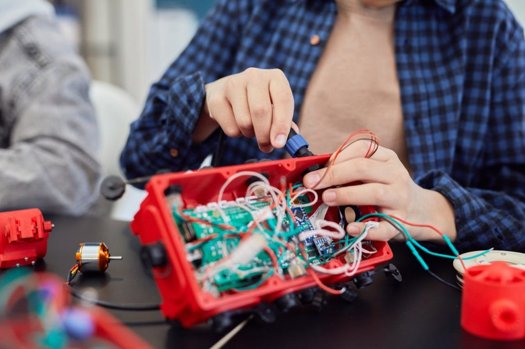 pexels-photo-7868884 Close-up of hands assembling a robotic project with wires and circuits.